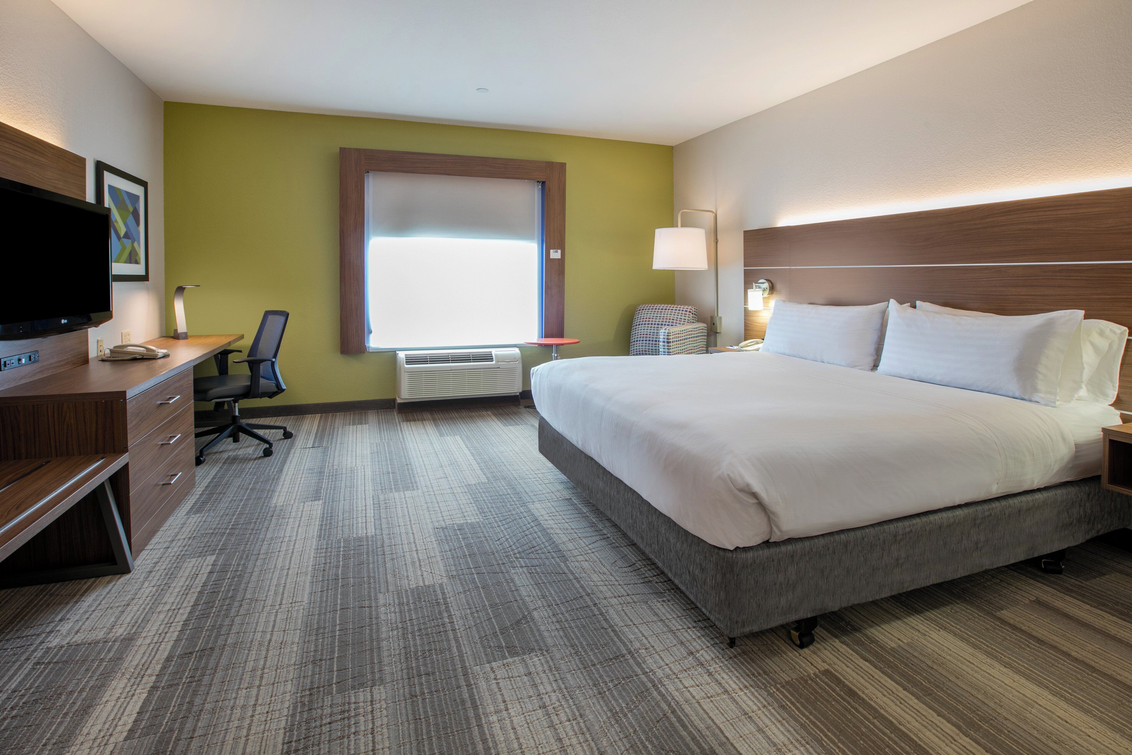 A hotel room with a bed, desk, chair, and a television.