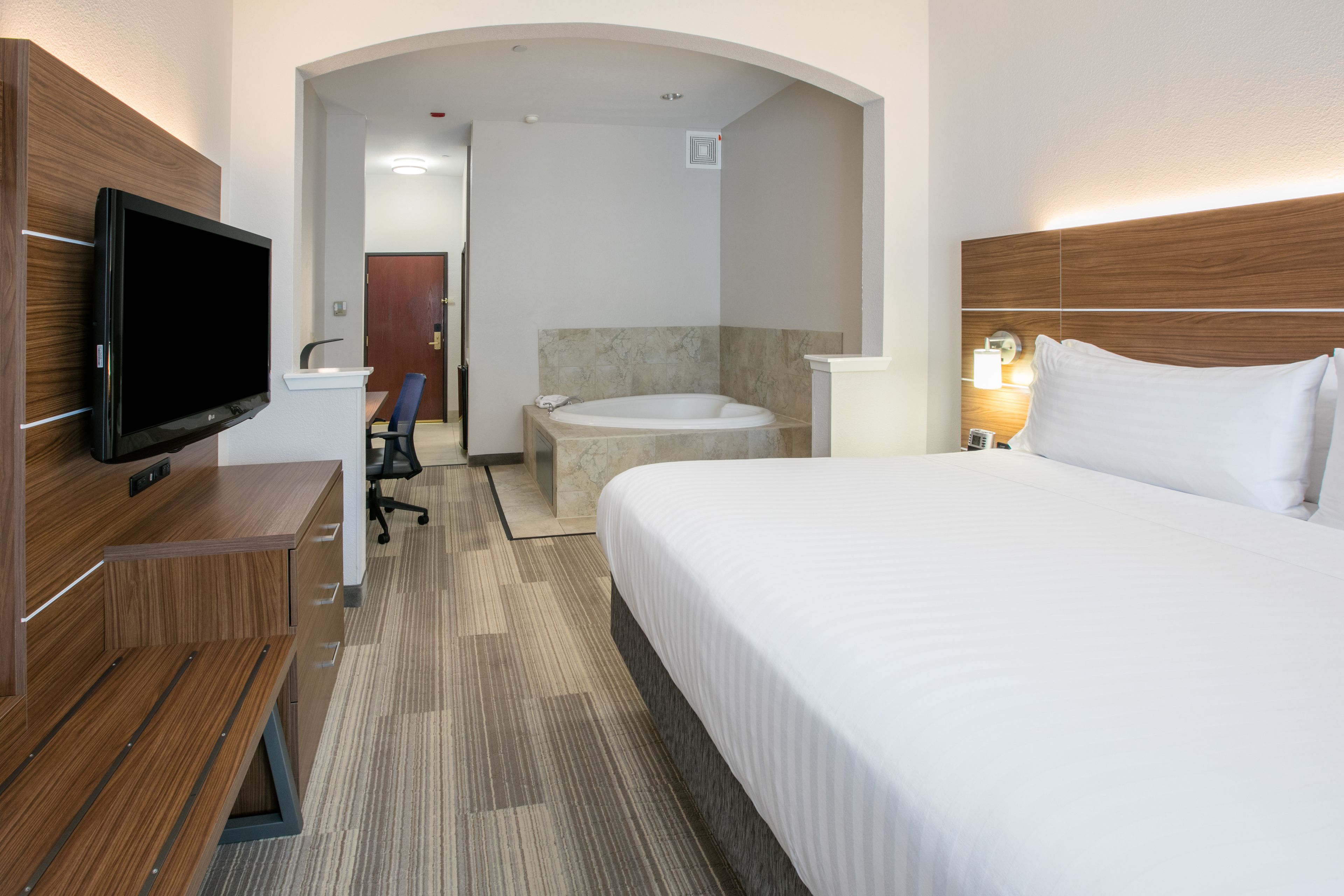A hotel room with a bed, a desk with a TV, a bathroom with a bathtub, and a shower.