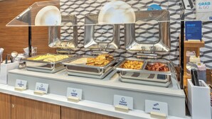Un buffet proposant différents plats présentés dans des plateaux étiquetés : œufs brouillés, fromage blanc et fromage brun, sauce aux saucisses, saucisses de dinde et bacon.