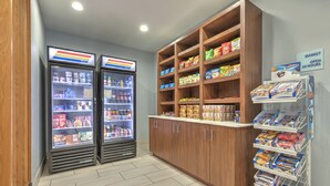 A self-service snack area with refrigerated beverage dispensers, a variety of packaged snacks, and a sign indicating the market is open 24 hours. - Holiday Inn Express Hotel & Suites Dallas-Grand Prairie I-20 by IHG (Grand Prairie)