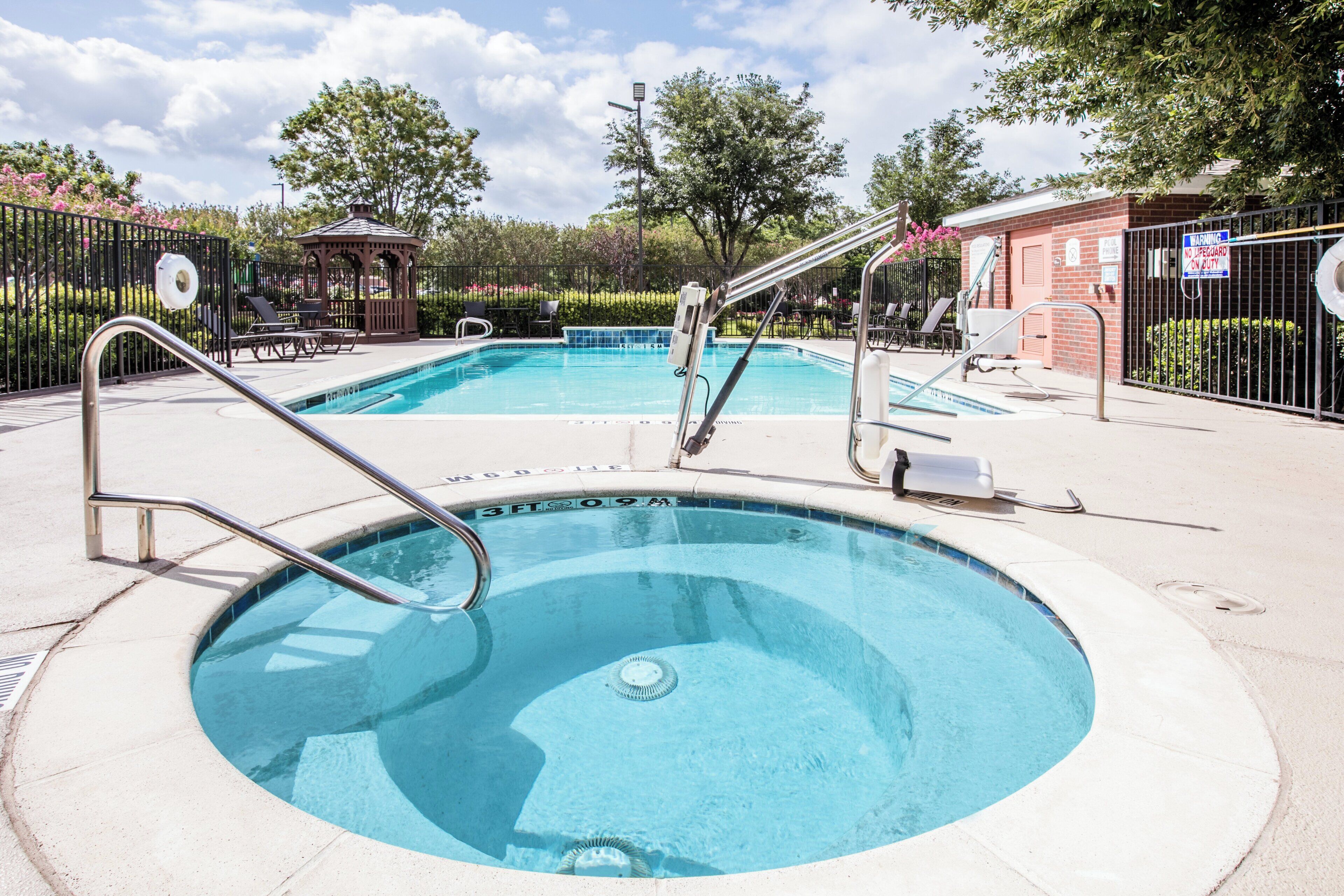 Une piscine avec un plongeoir, entourée de chaises longues et d’un kiosque.