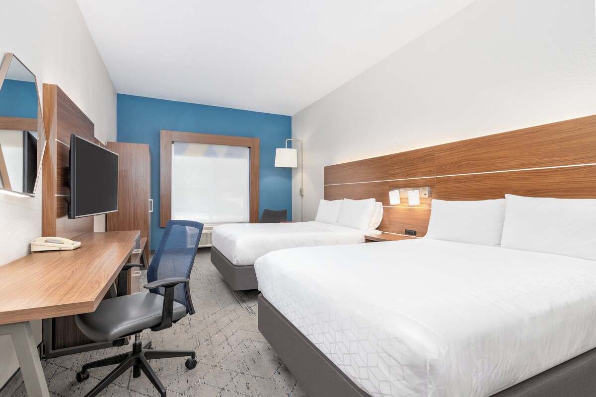 Een hotelkamer met twee bedden, een bureau met stoel, een televisie en een raam.