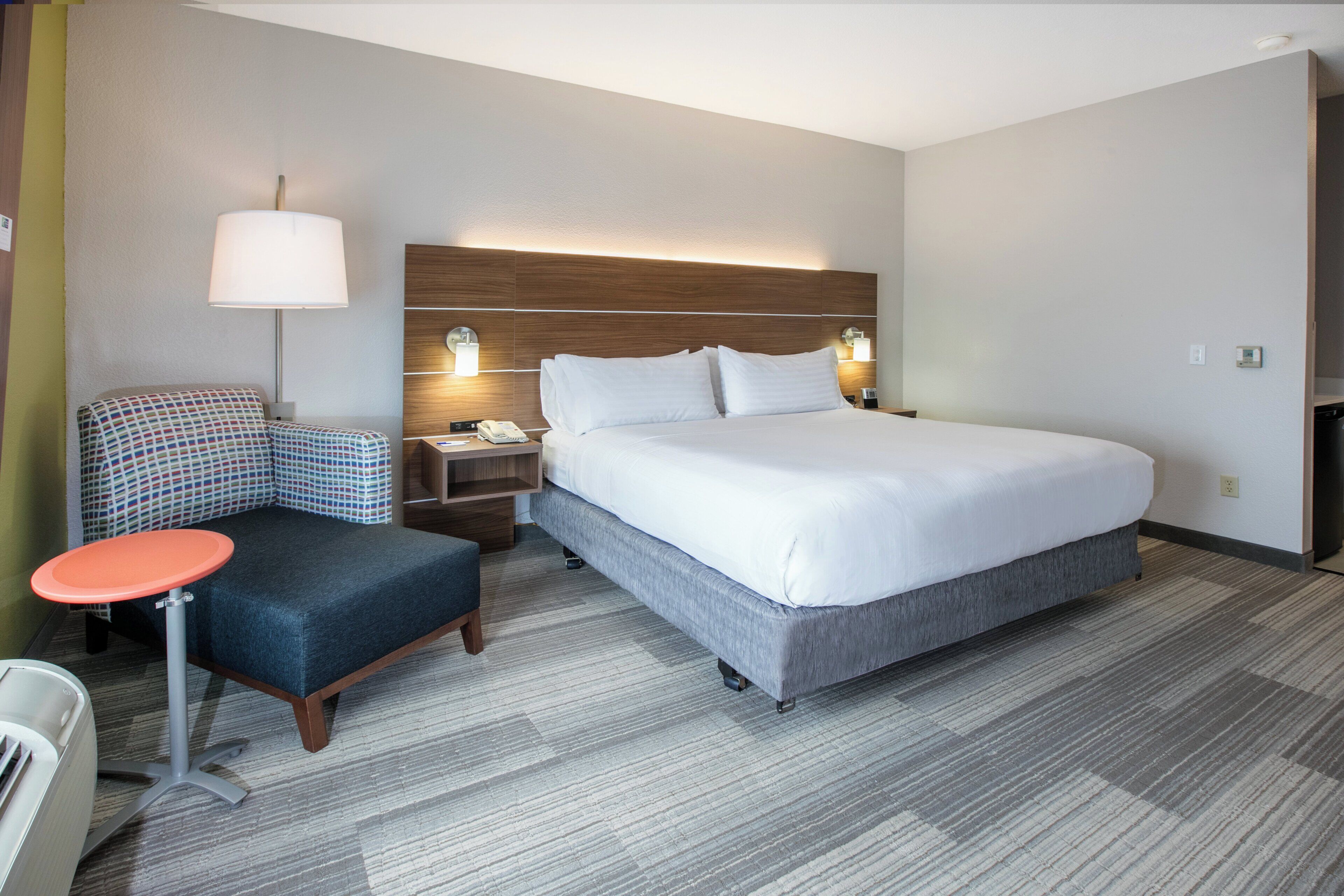 Une chambre d’hôtel avec un lit, un bureau, une chaise, une lampe et une table de chevet.