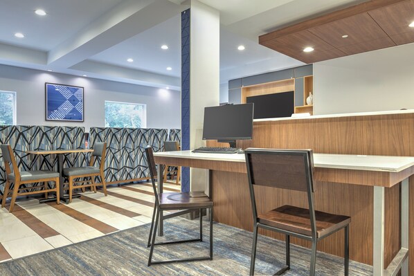 Een moderne hotel lobby met een receptiebalie, een zithoek en grote ramen.
