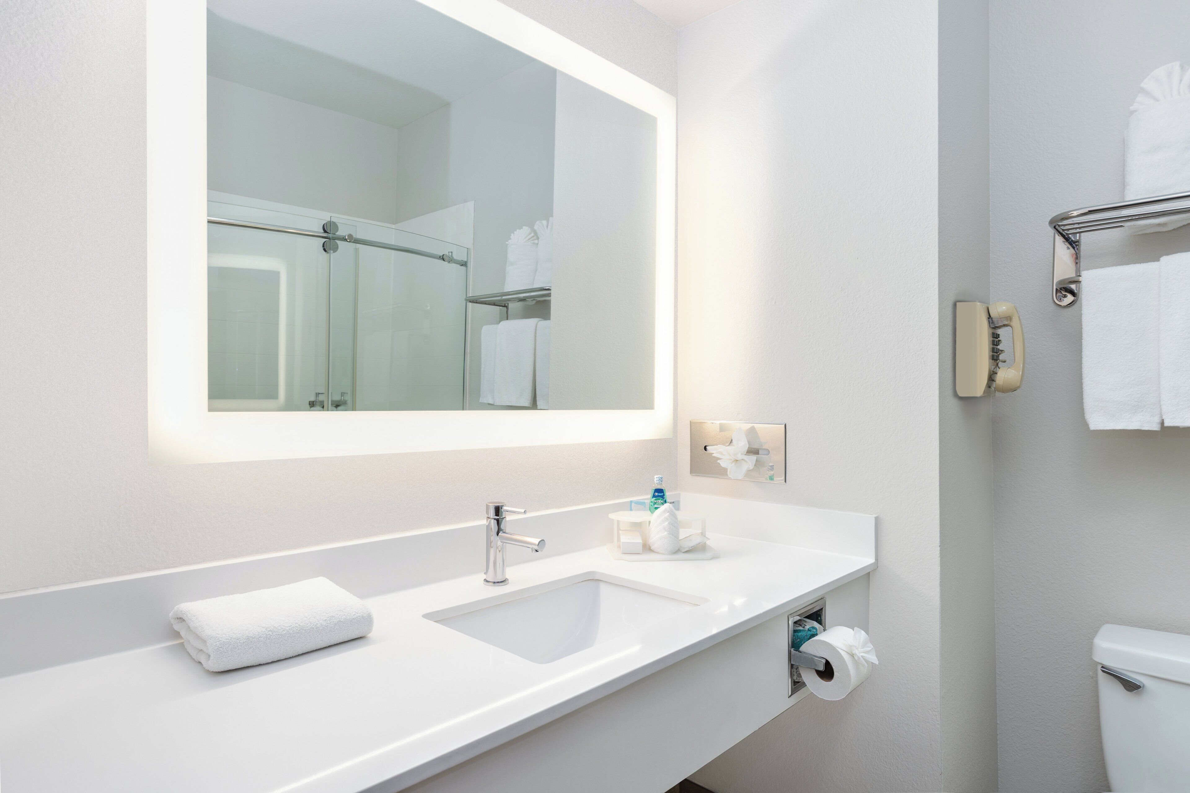 A modern bathroom with a large mirror, two sinks, a toilet, and a towel rack.