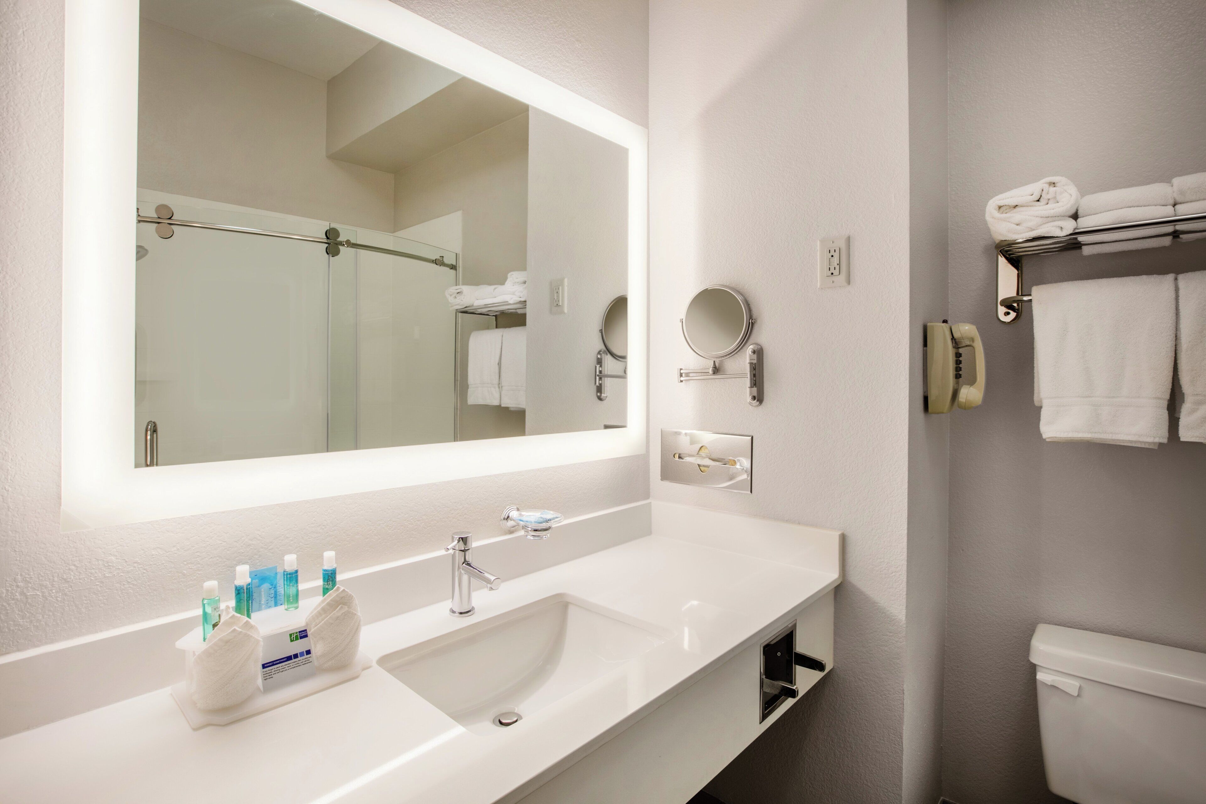 A modern bathroom with a large mirror, a sink, and a toilet.