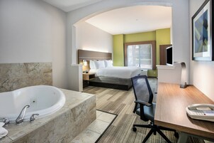 Quarto de hotel com uma banheira grande, uma cama, uma escrivaninha com telefone e uma cadeira.