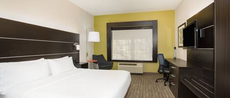A hotel room with a large bed, a desk with a computer, a TV, and a window with a view.