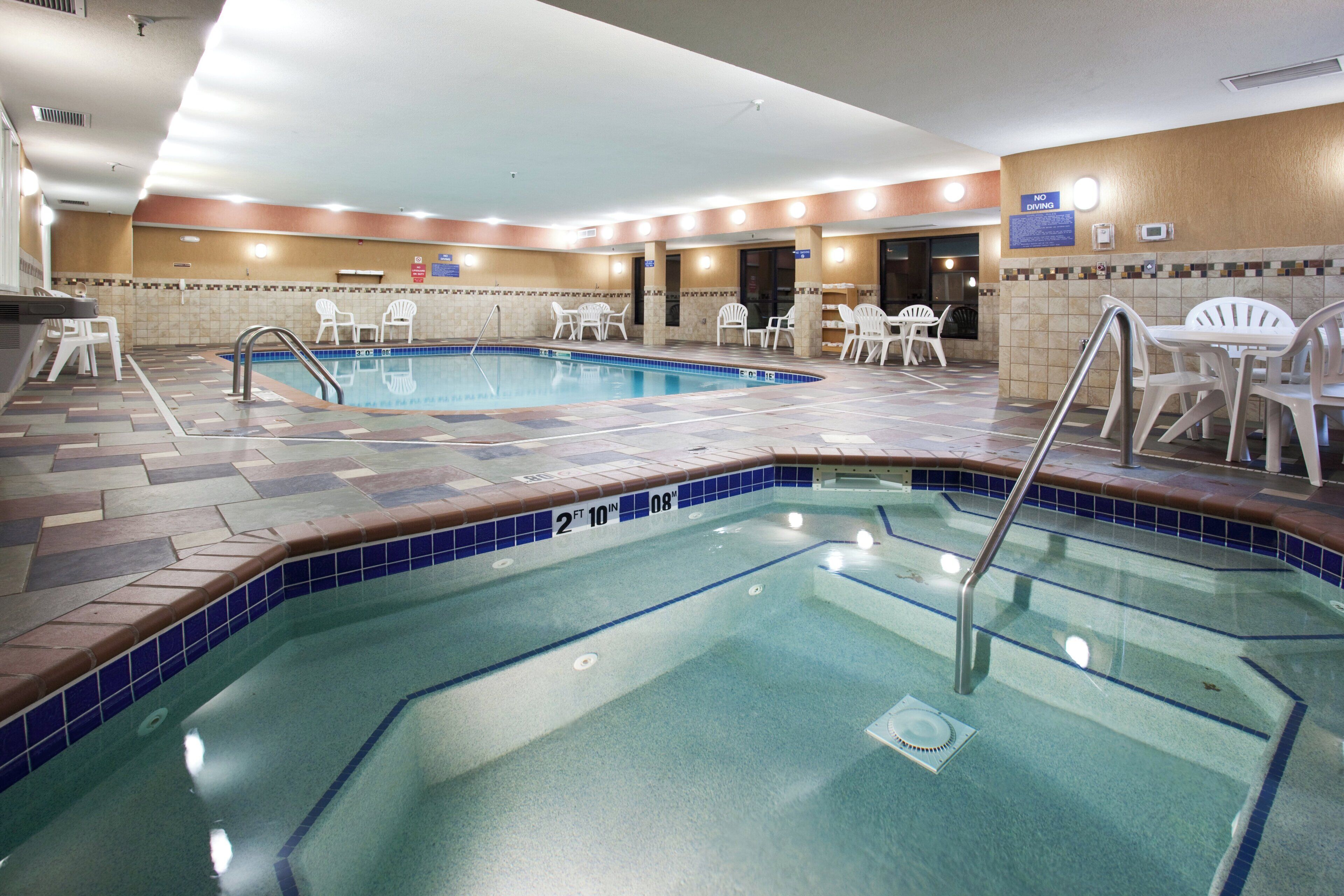Una piscina interior con borde de azulejos, rodeada de sillas y mesas de plástico blanco, y un cartel de 'No Diving' en la pared.