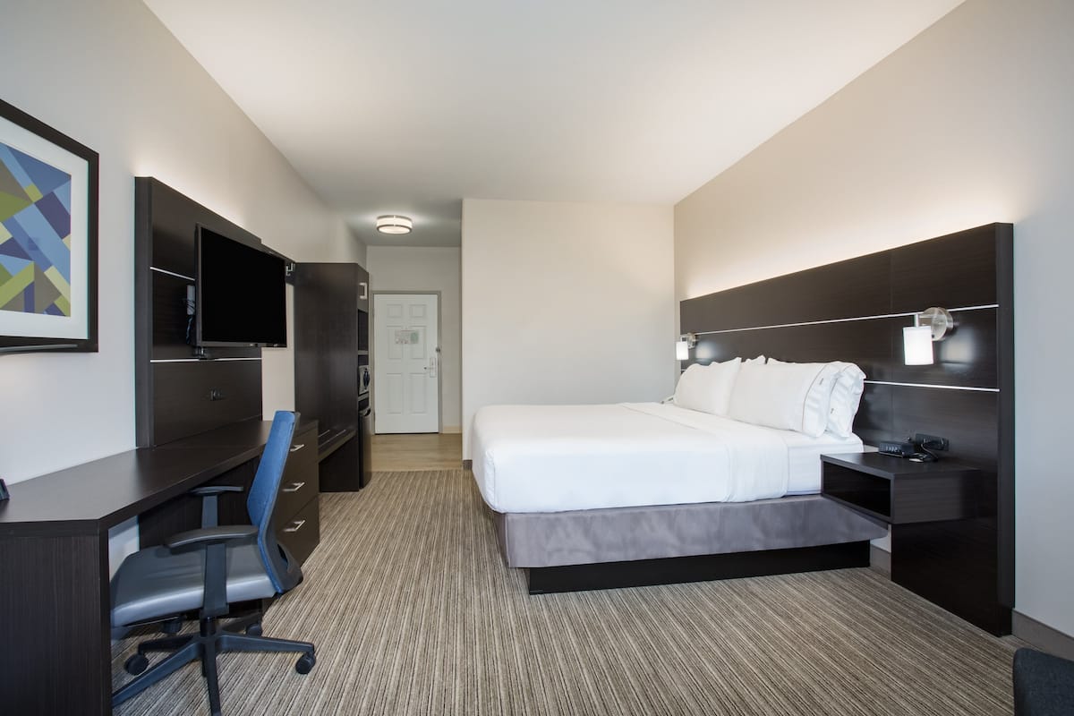 Quarto de hotel moderno com cama, escrivaninha, cadeira e televisão de tela plana.