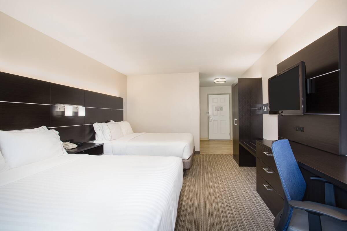 Quarto de hotel com duas camas, uma escrivaninha com cadeira, televisão e guarda-roupa.