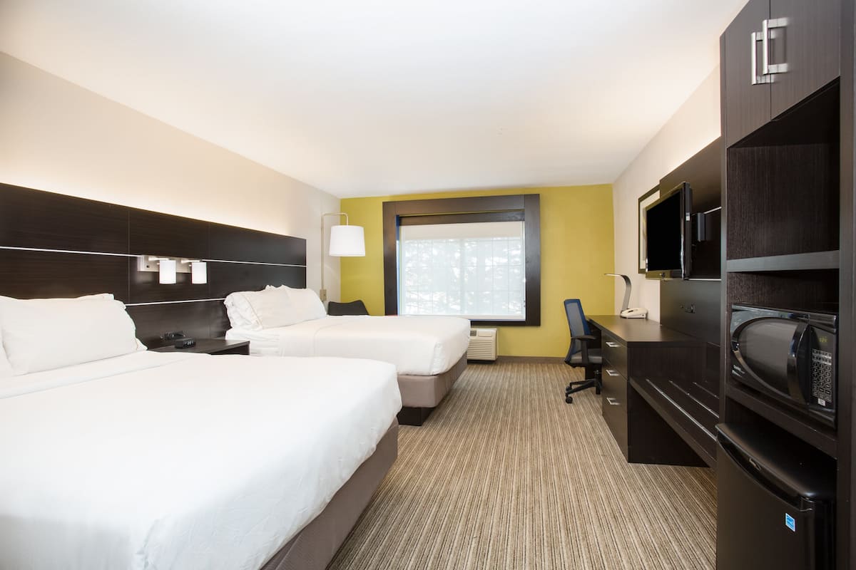 Quarto de hotel com duas camas, uma escrivaninha com computador, televisão e micro-ondas.