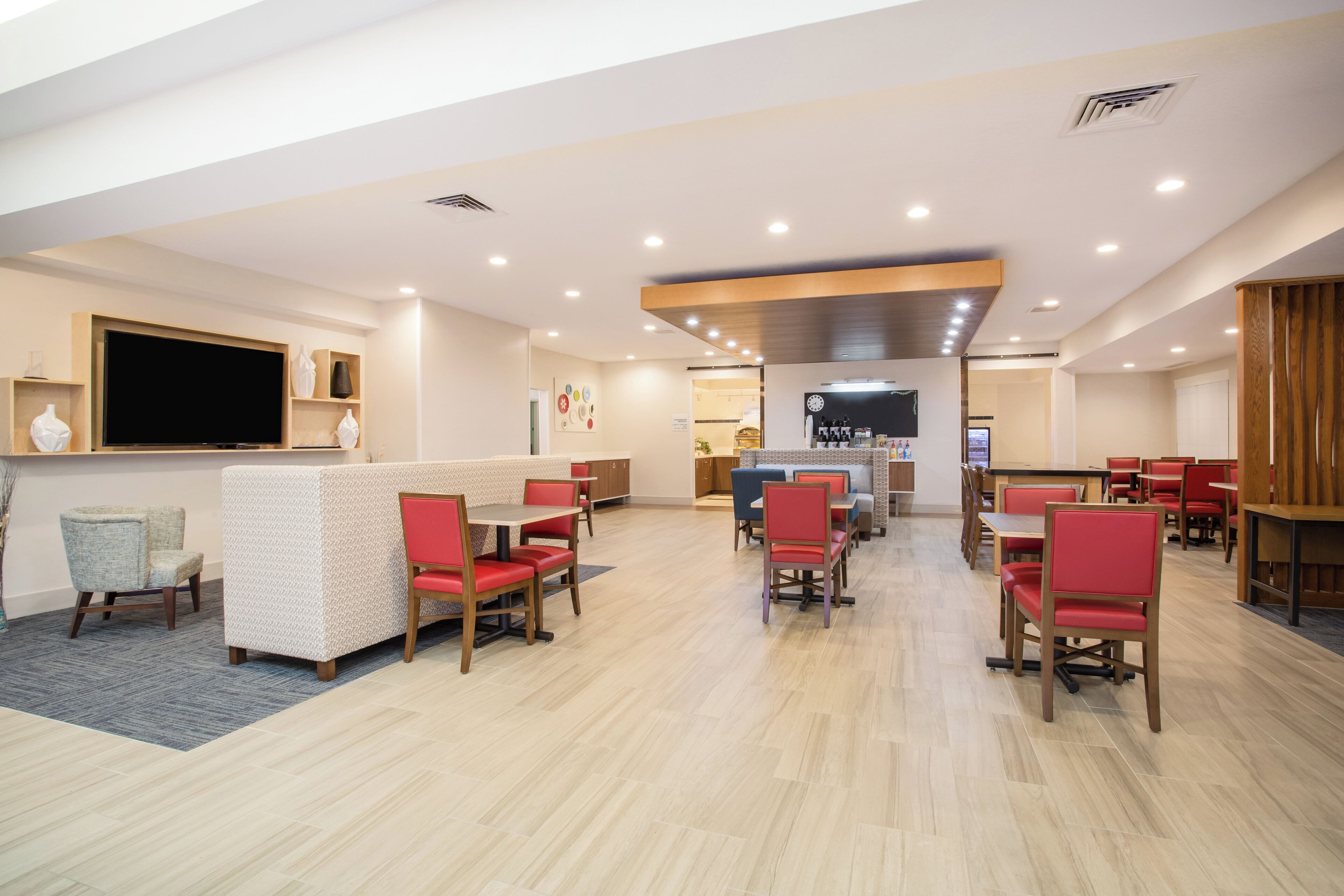 Un grand espace intérieur aménagé avec différents types de sièges, notamment des banquettes et des tables, ainsi qu’un téléviseur fixé au mur.