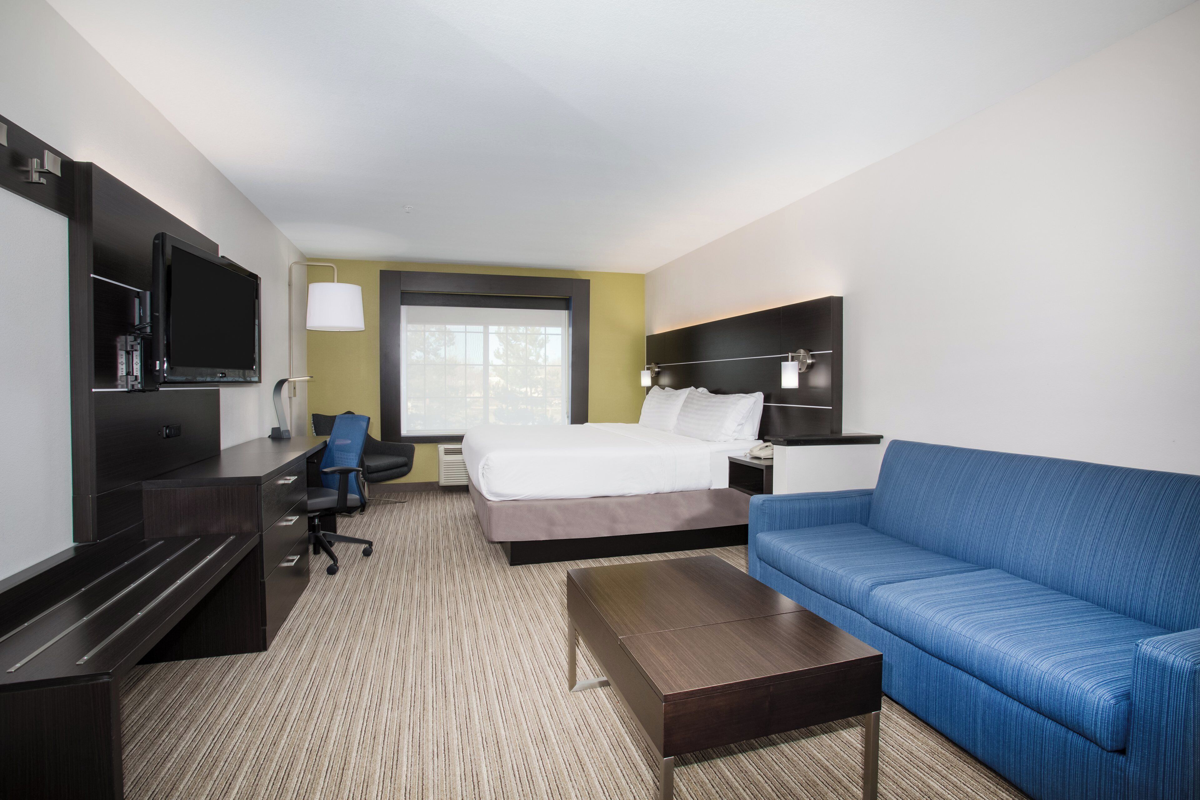 A hotel room with a bed, a desk with a TV, a blue sofa, and a coffee table.