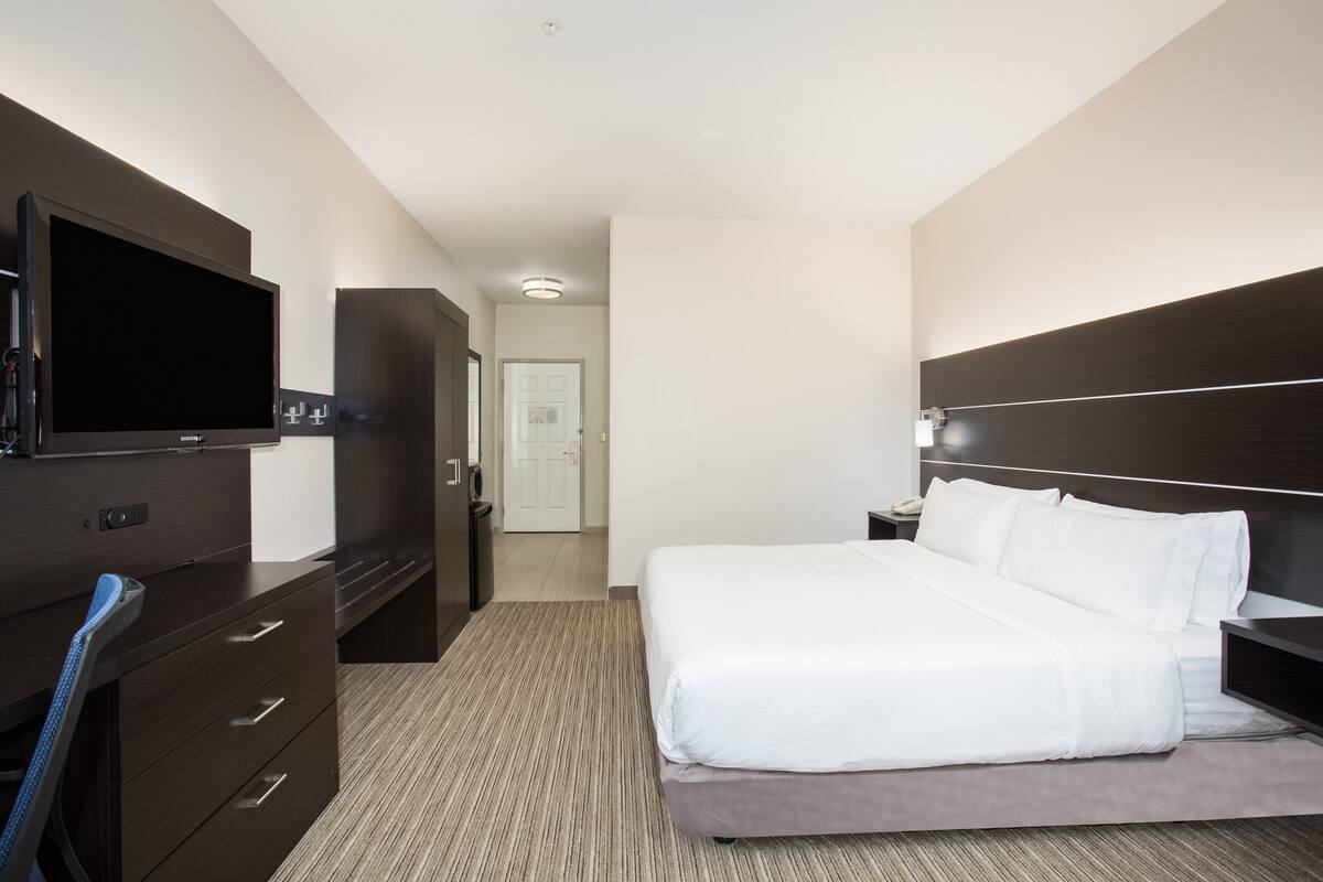 Quarto de hotel com uma cama, uma secretária com televisão de ecrã plano, um guarda-roupa e uma porta que dá para outro quarto.