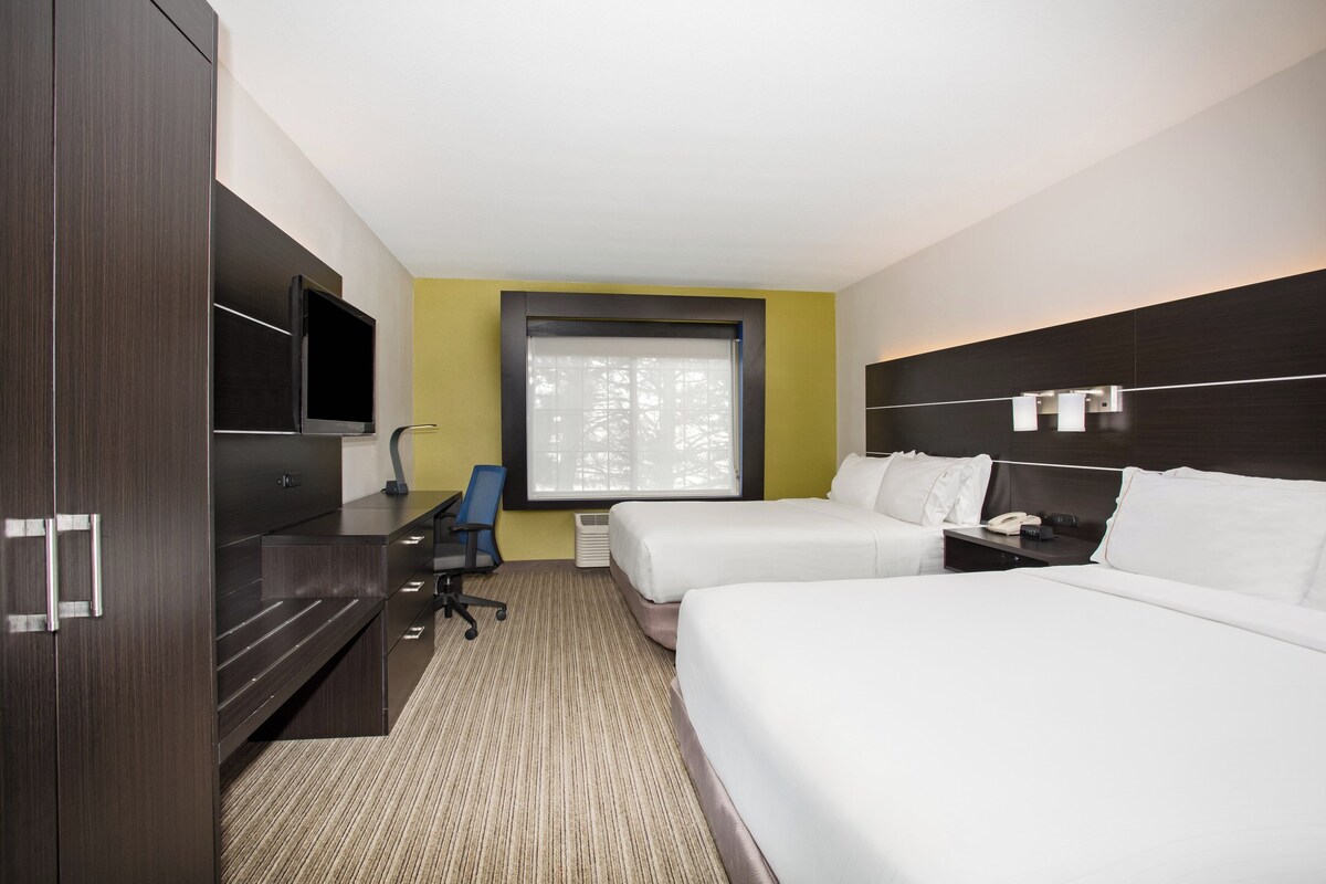 Une chambre d’hôtel avec deux lits, un bureau, une télévision et une fenêtre avec des stores.