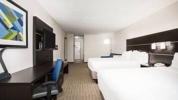 A hotel room with a desk, chair, television, two beds, and a door leading to another room.