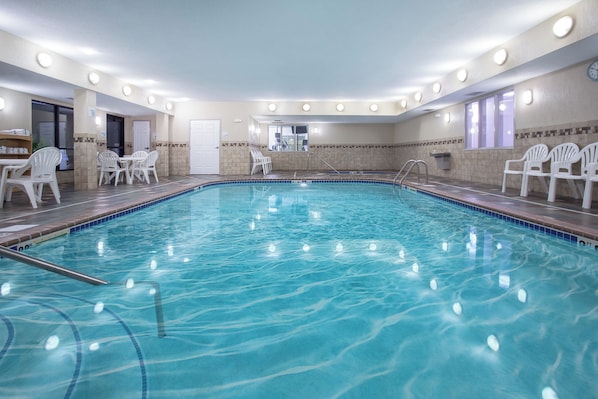 A swimming pool with a tiled edge, surrounded by white chairs and a sunbed.