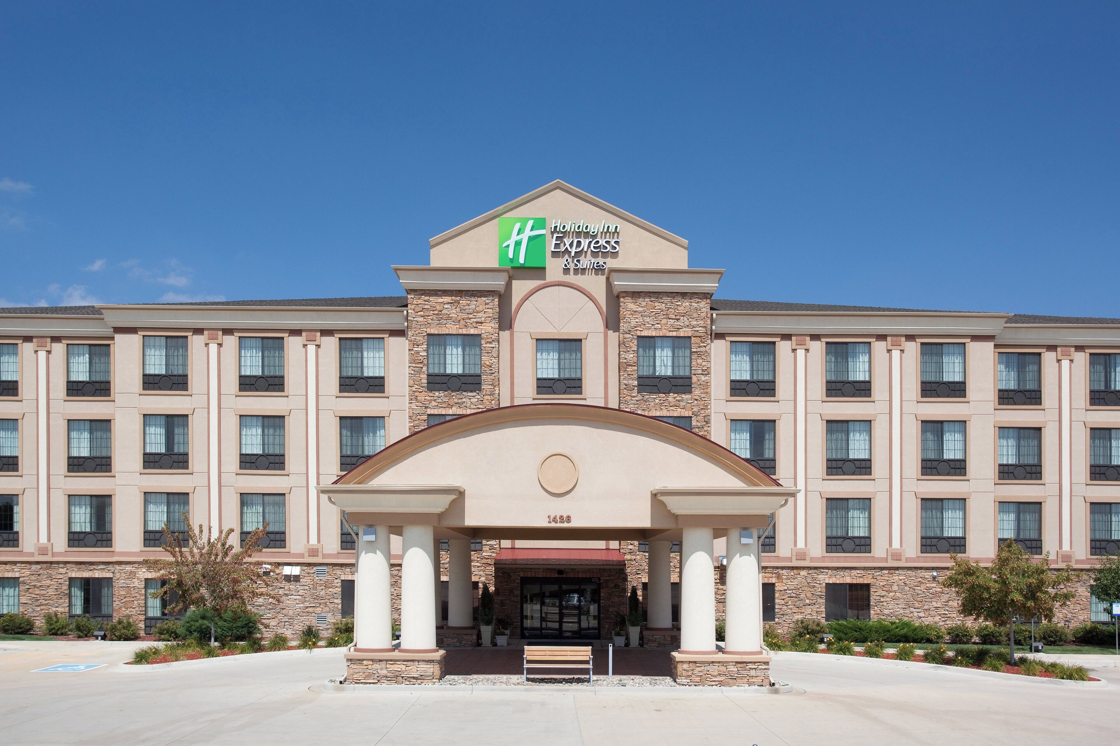 Un hôtel Holiday Inn Express & Suites doté d’une façade en pierre, de nombreuses fenêtres et d’une entrée centrale ornée de colonnes.