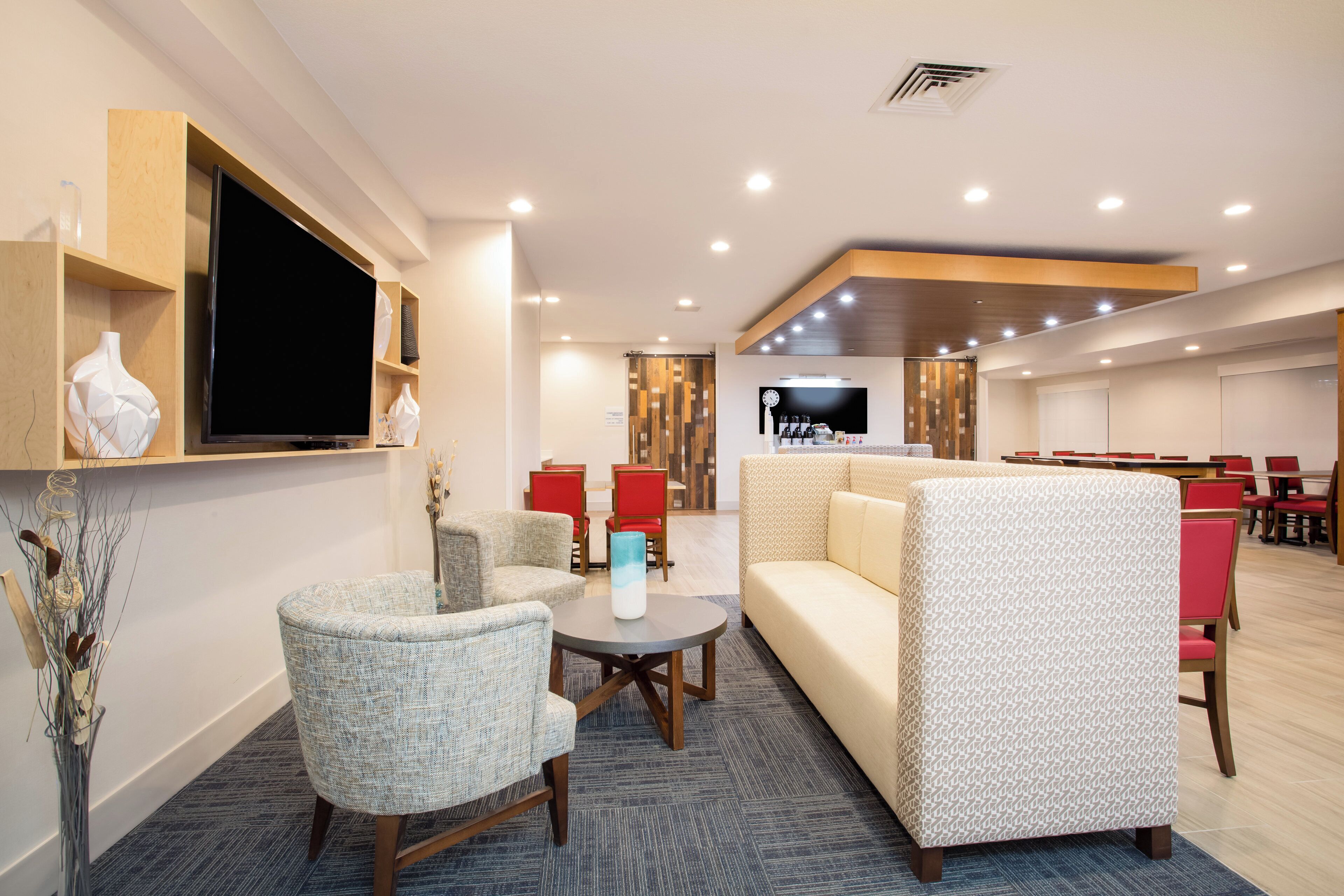A hotel lobby with seating, a television, and a dining area.