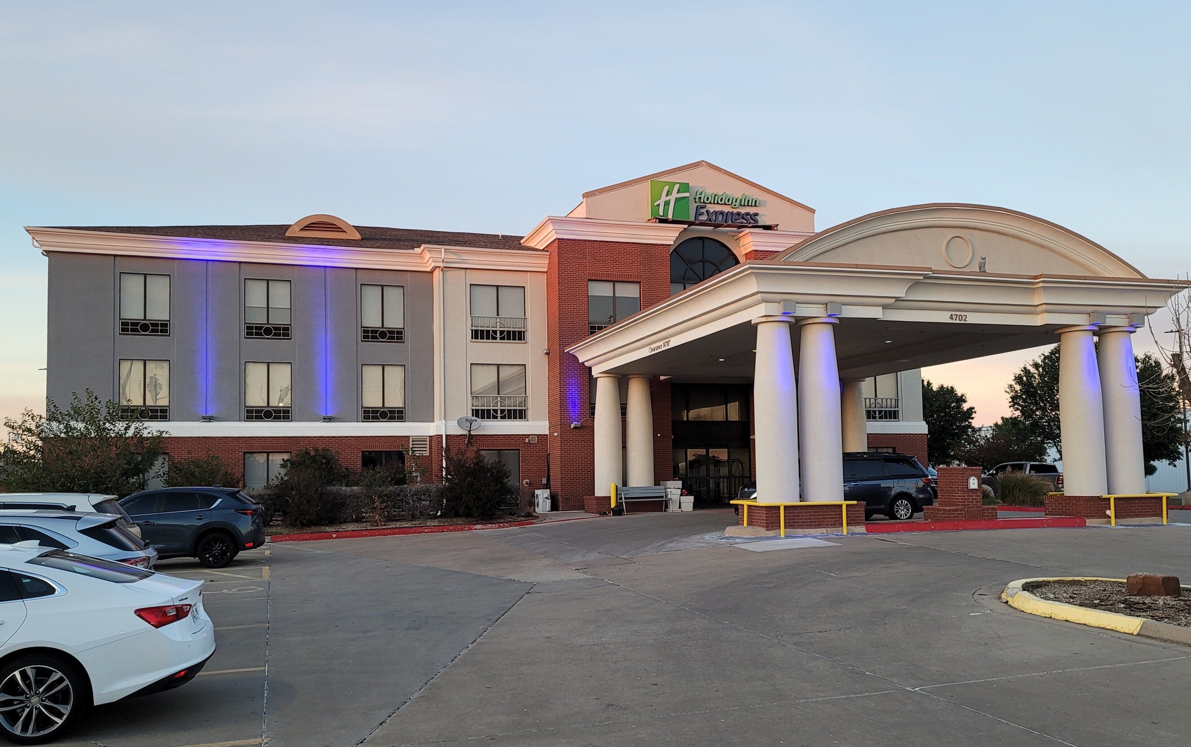 A Holiday Inn Express hotel with a modern facade, a covered entrance, and a parking lot with several cars.