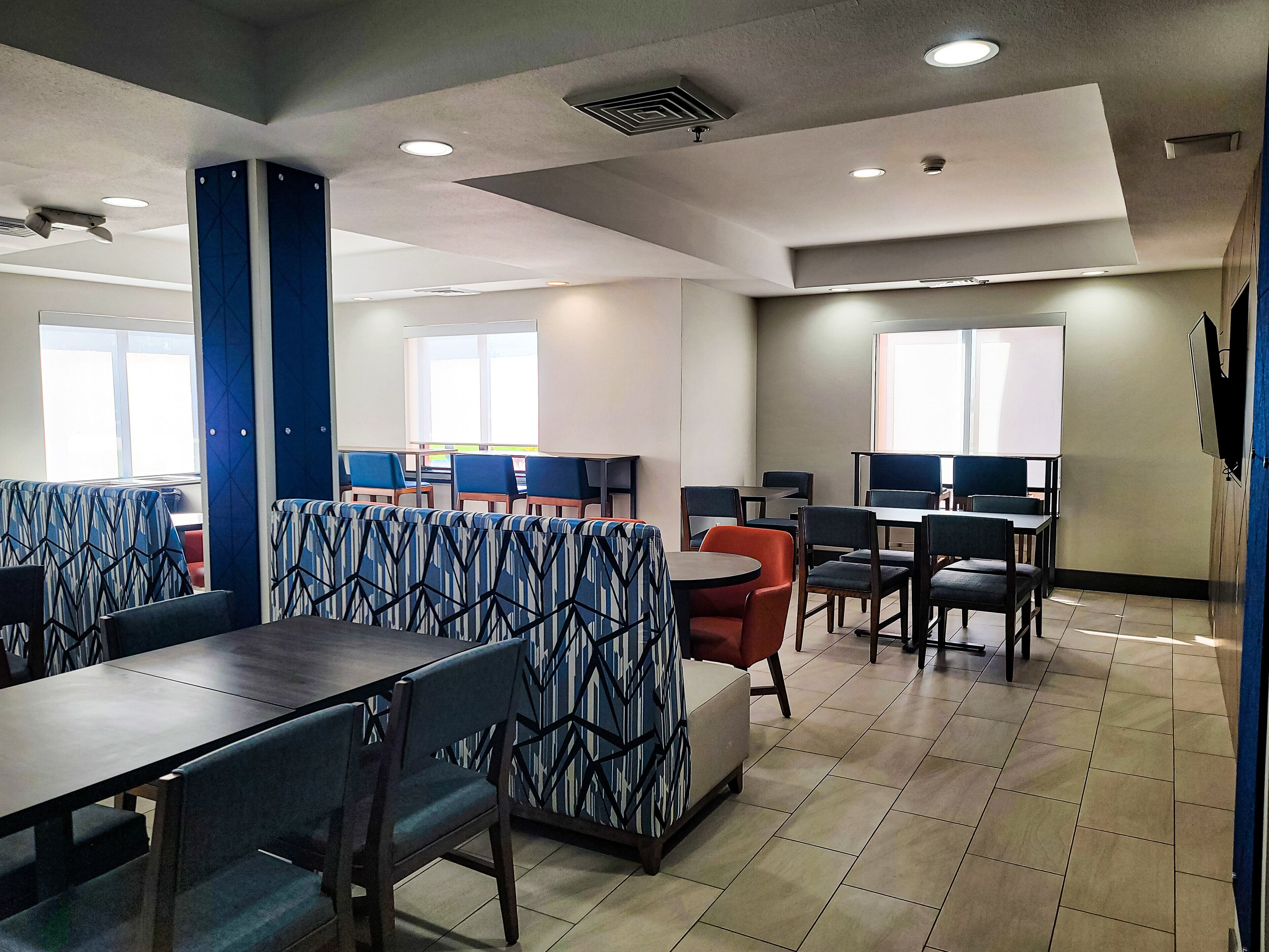 A modern hotel lobby with seating areas, a reception desk, and a large TV screen.