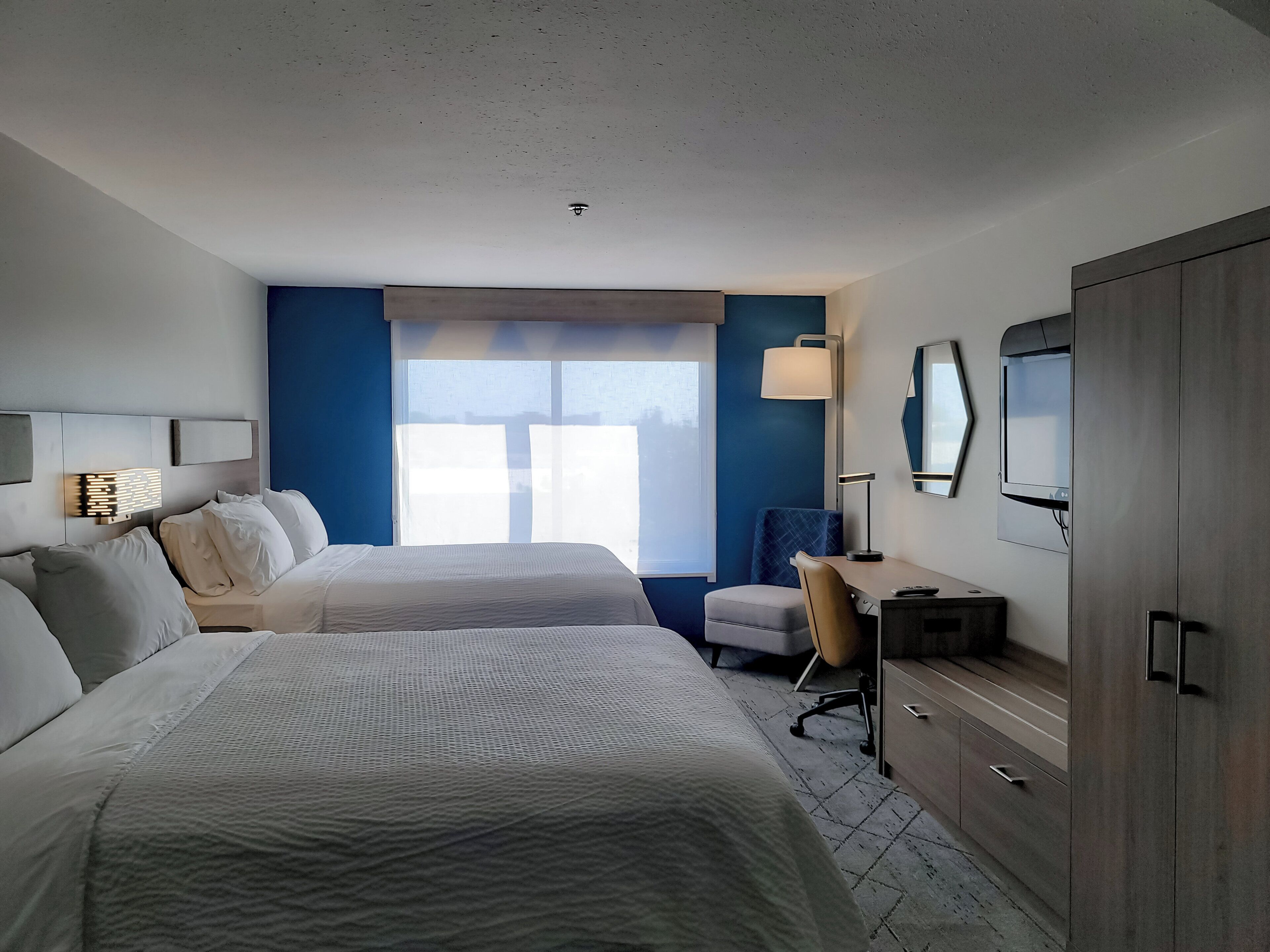 Une chambre d’hôtel avec deux lits, un bureau, une chaise, une télévision et une armoire.