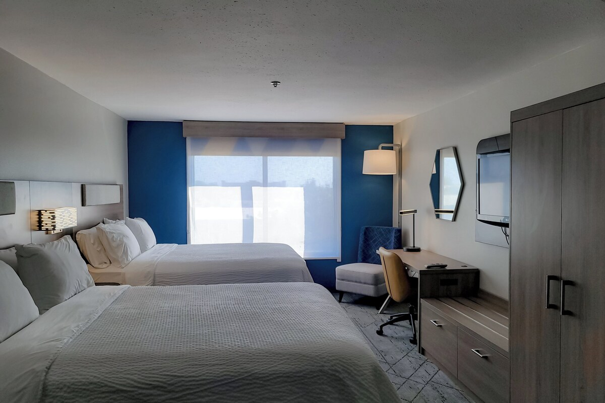 A hotel room with two beds, a desk, a chair, a TV, and a wardrobe.