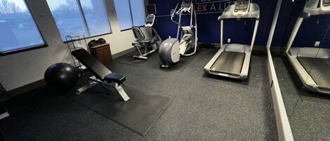 Une salle de sport équipée de matériel d’exercice, d’un banc et d’un mur orné de messages motivants.