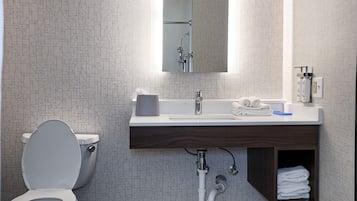 Une salle de bain moderne équipée de toilettes, d’un lavabo, d’un miroir et d’une poubelle.