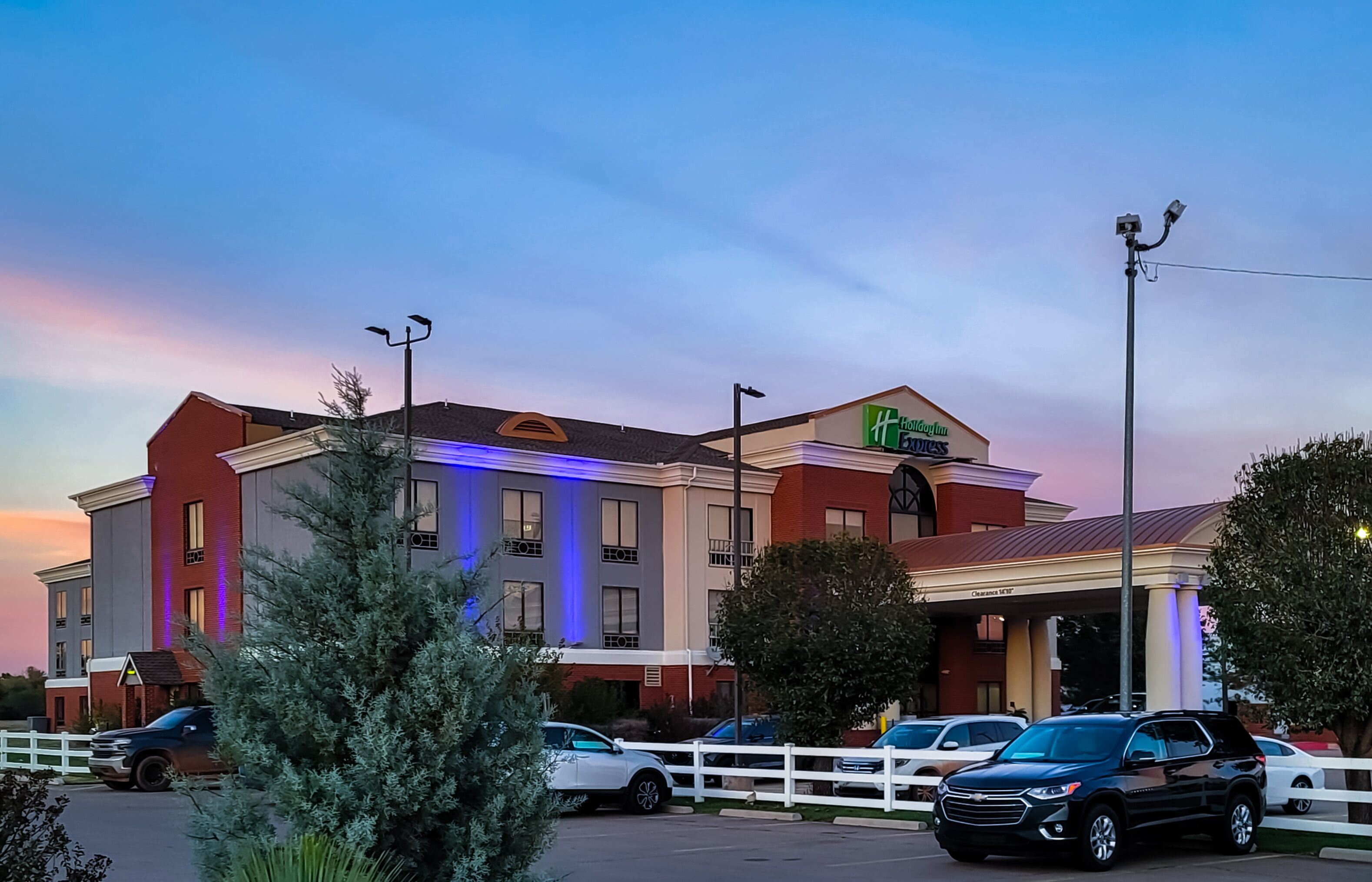 Un hotel con fachada moderna, varios espacios de estacionamiento y una entrada bien iluminada.