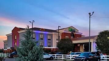 Un hotel con fachada moderna, varios espacios de estacionamiento y una entrada bien iluminada.