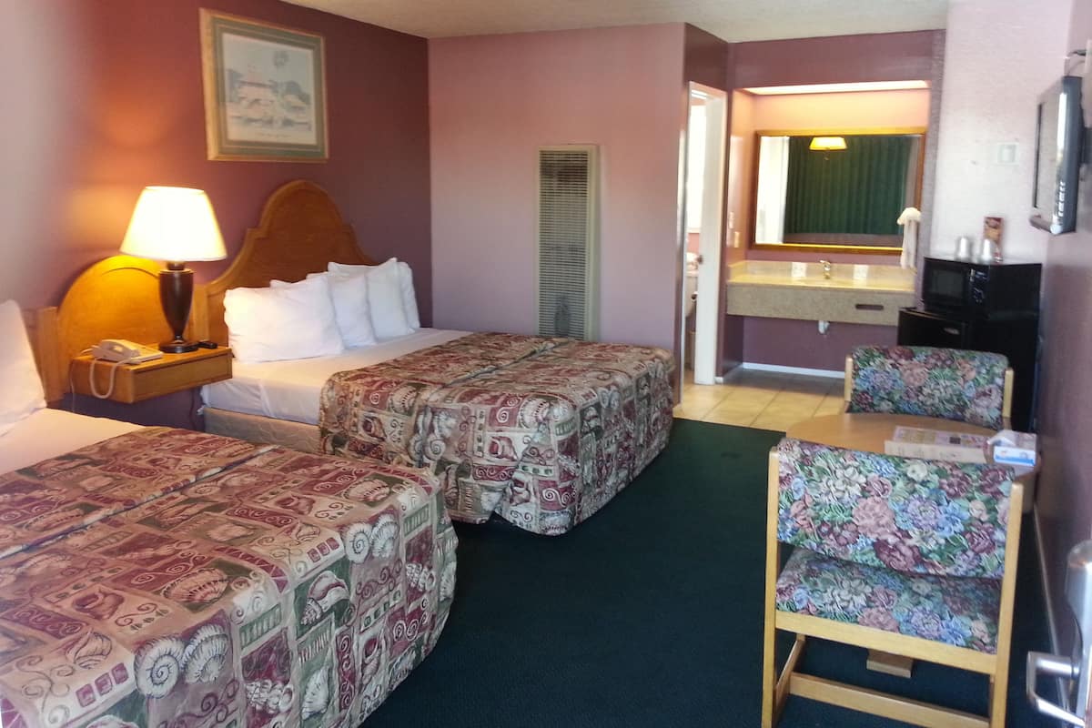 A hotel room with two beds, a desk, a chair, a lamp, a telephone, a mirror, and a television.