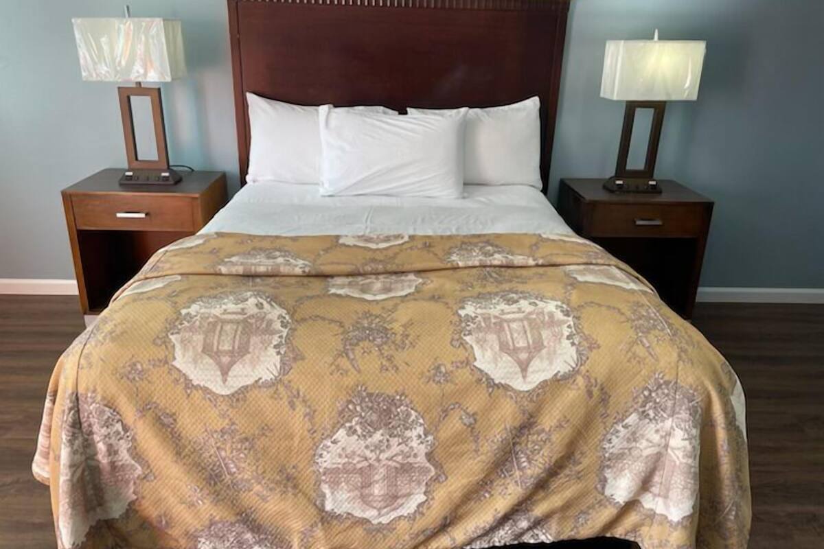 A neatly made bed with a patterned bedspread, two bedside tables with lamps, and a wooden headboard.
