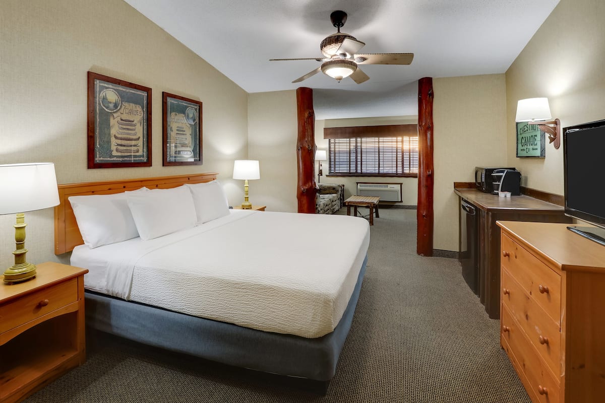 Habitación de hotel con cama, mesitas de noche, escritorio, televisor y ventilador de techo.