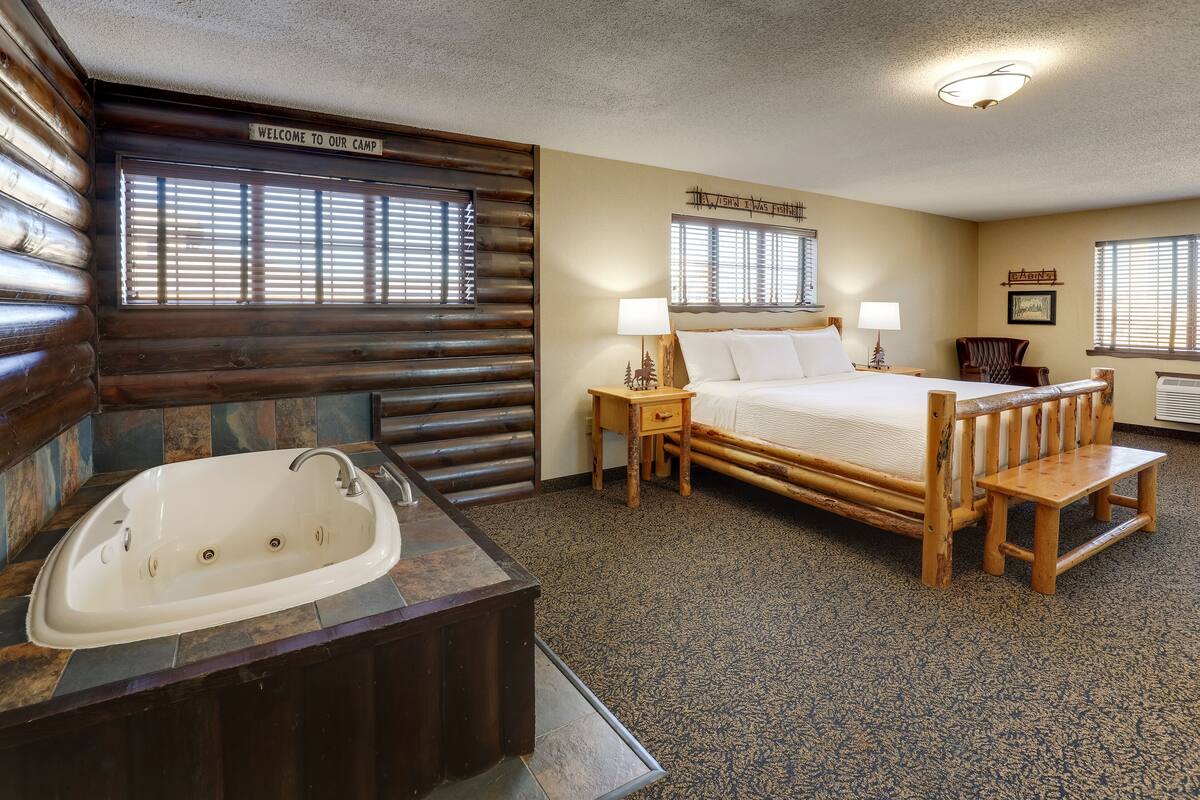 Un dormitorio tipo cabaña con una cama grande, un banco de madera, un lavabo y una ventana con persianas.