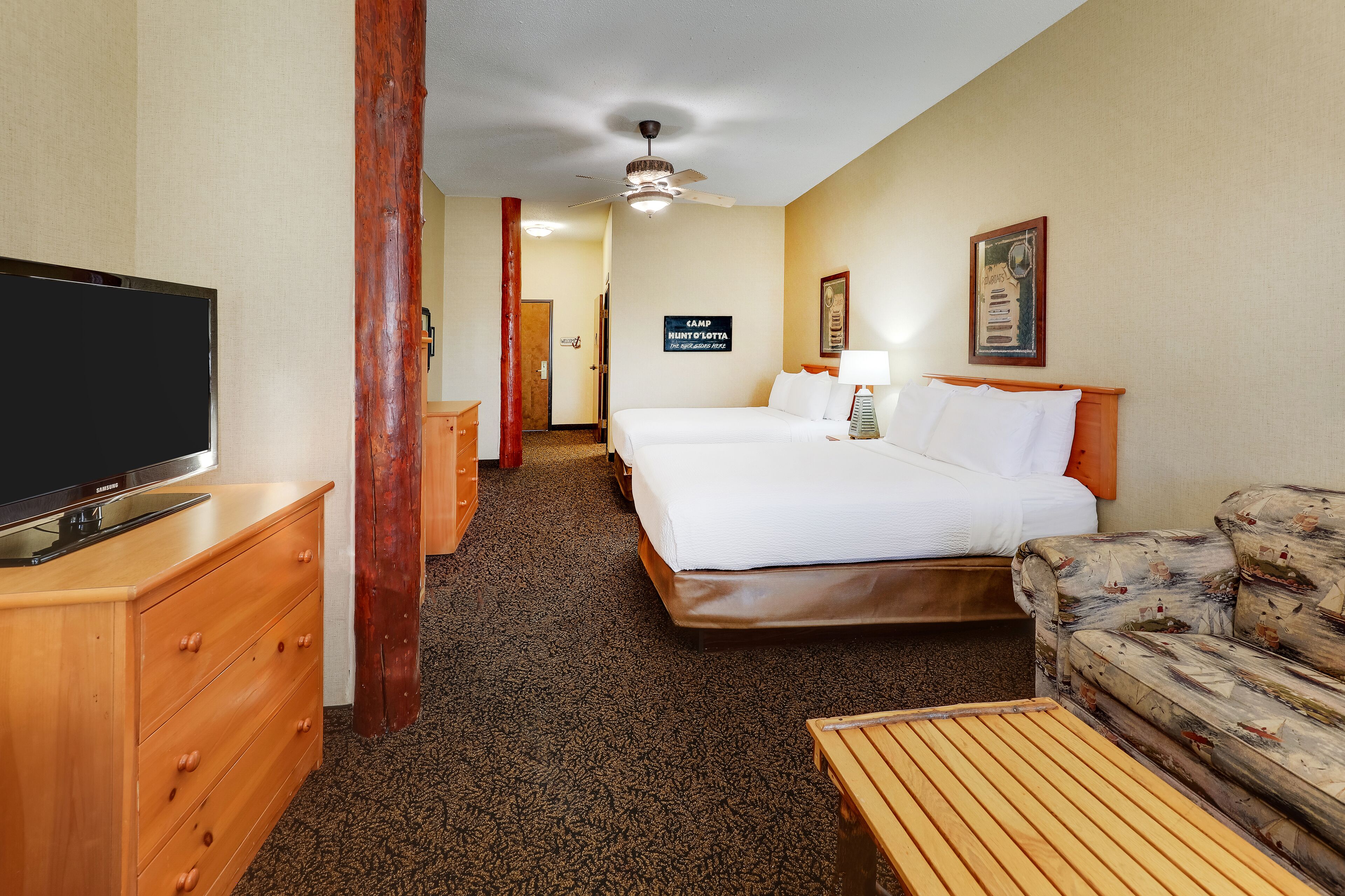 A hotel room with a bed, a sofa, a TV, a wooden dresser, and a ceiling fan.