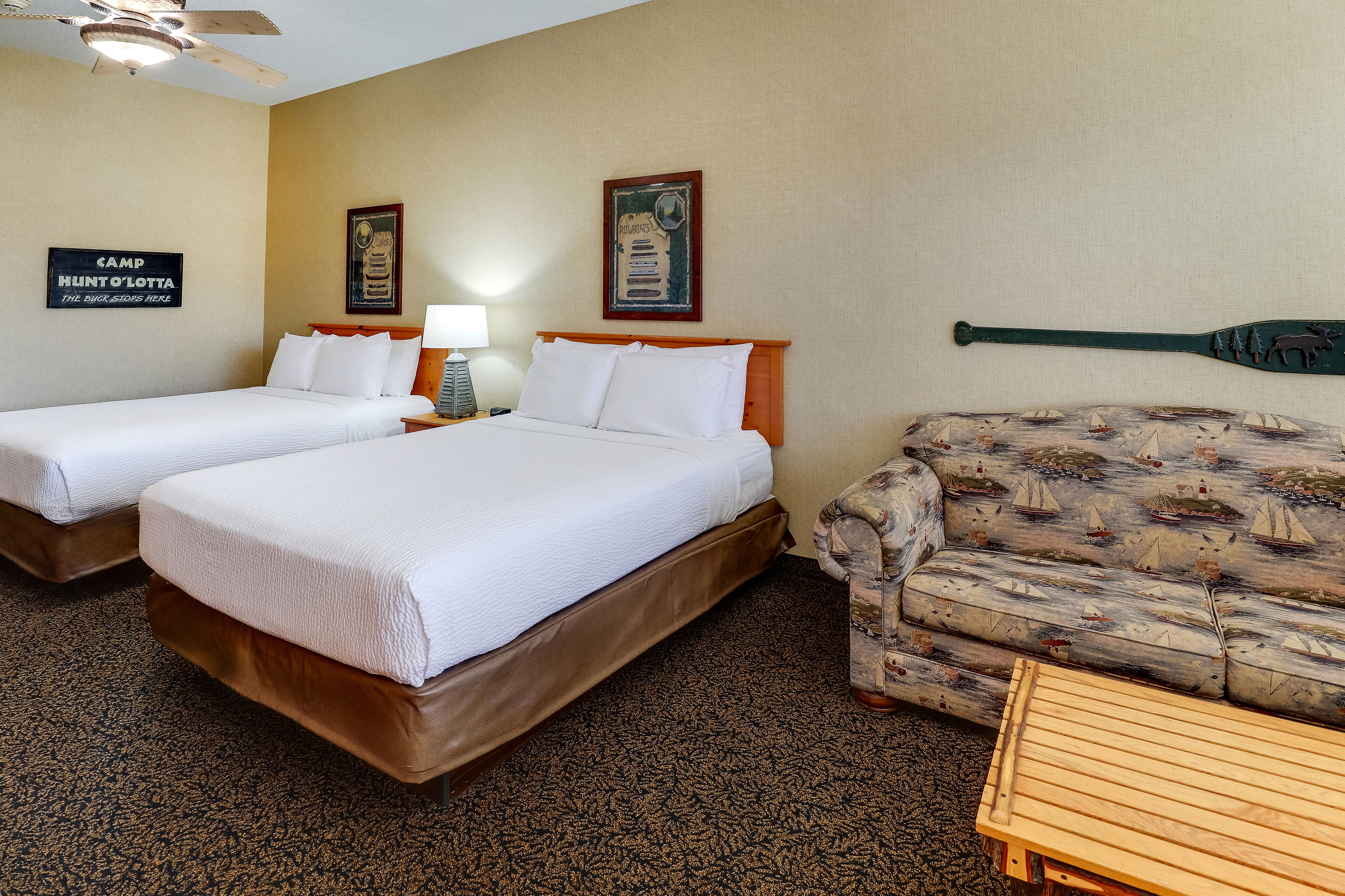 Ein Hotelzimmer mit zwei Betten, einer Couch, einem Holztisch und einem Deckenventilator.