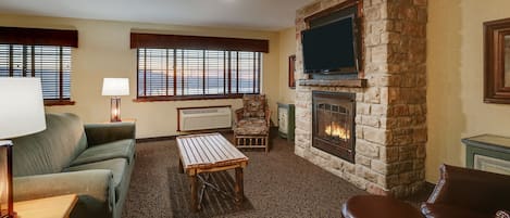 A living room with a stone fireplace, a sofa, a coffee table, and a TV mounted on the wall.