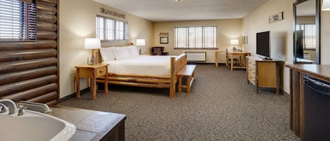 A hotel room with a bed, a desk, a chair, a TV, a mirror, and a bathroom with a sink and a bathtub.