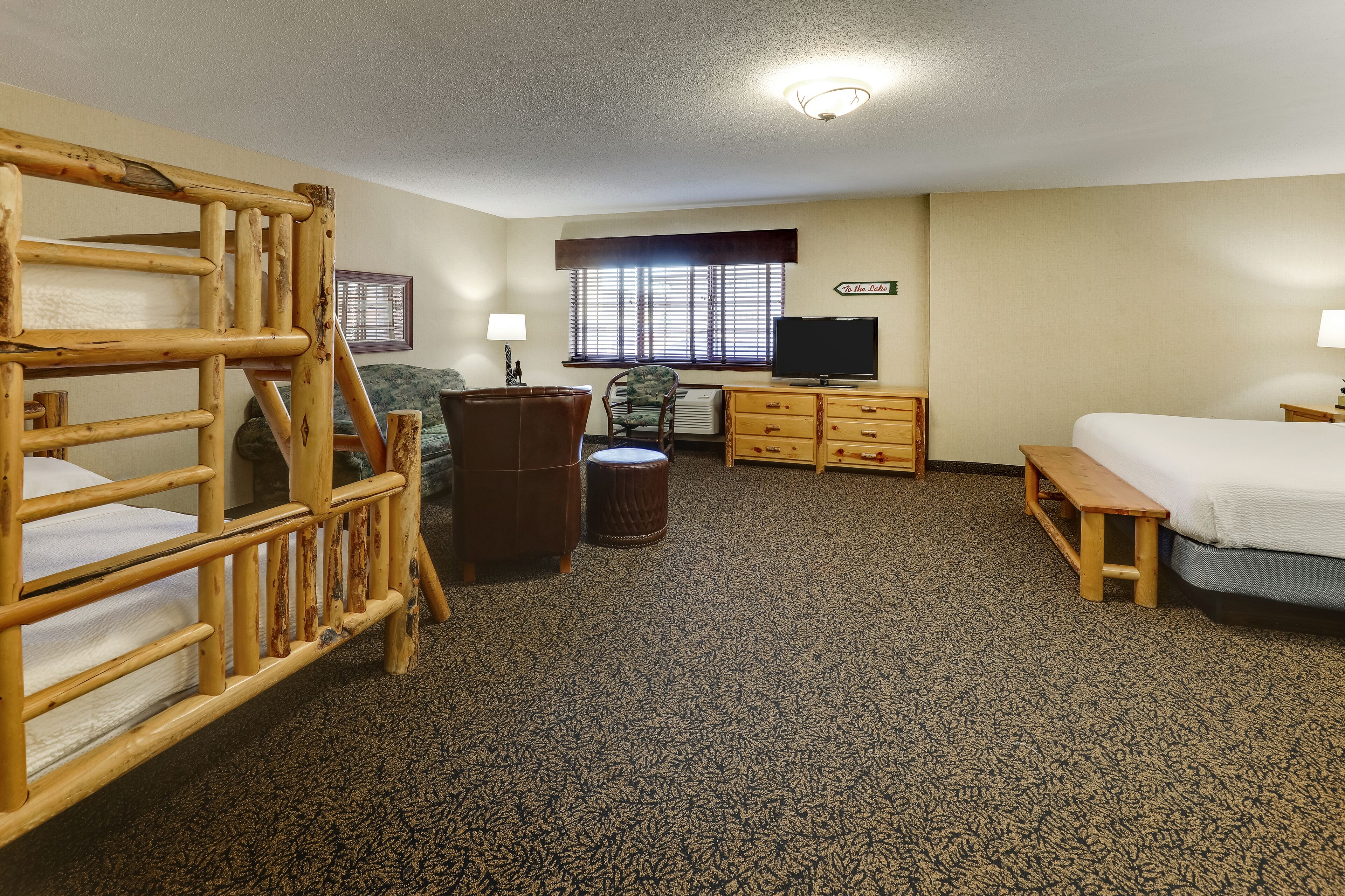 A room with bunk beds, a desk, a chair, a television, and a window with blinds.