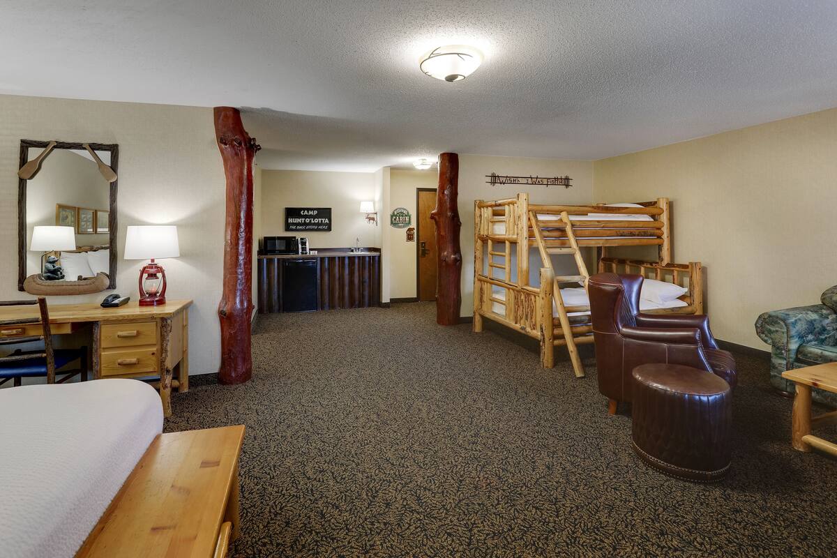 Una habitación de hotel con una cama litera de madera, un escritorio con lámpara, una silla y un espejo grande.