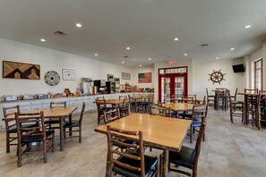 A spacious restaurant with wooden tables and chairs, a kitchen area, and various wall decorations including an American flag and a ship's wheel. - Stoney Creek Hotel Quad Cities - Moline (Moline)