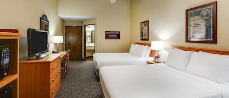 A hotel room with two beds, a TV, a desk with a lamp, and a ceiling fan.