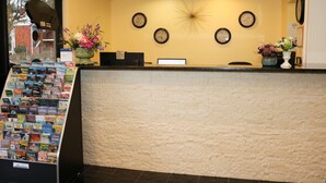 A reception area with a stone-textured counter, multiple clocks on the wall, and a display of travel brochures. - Shining Light Inn & Suites (Kissimmee)