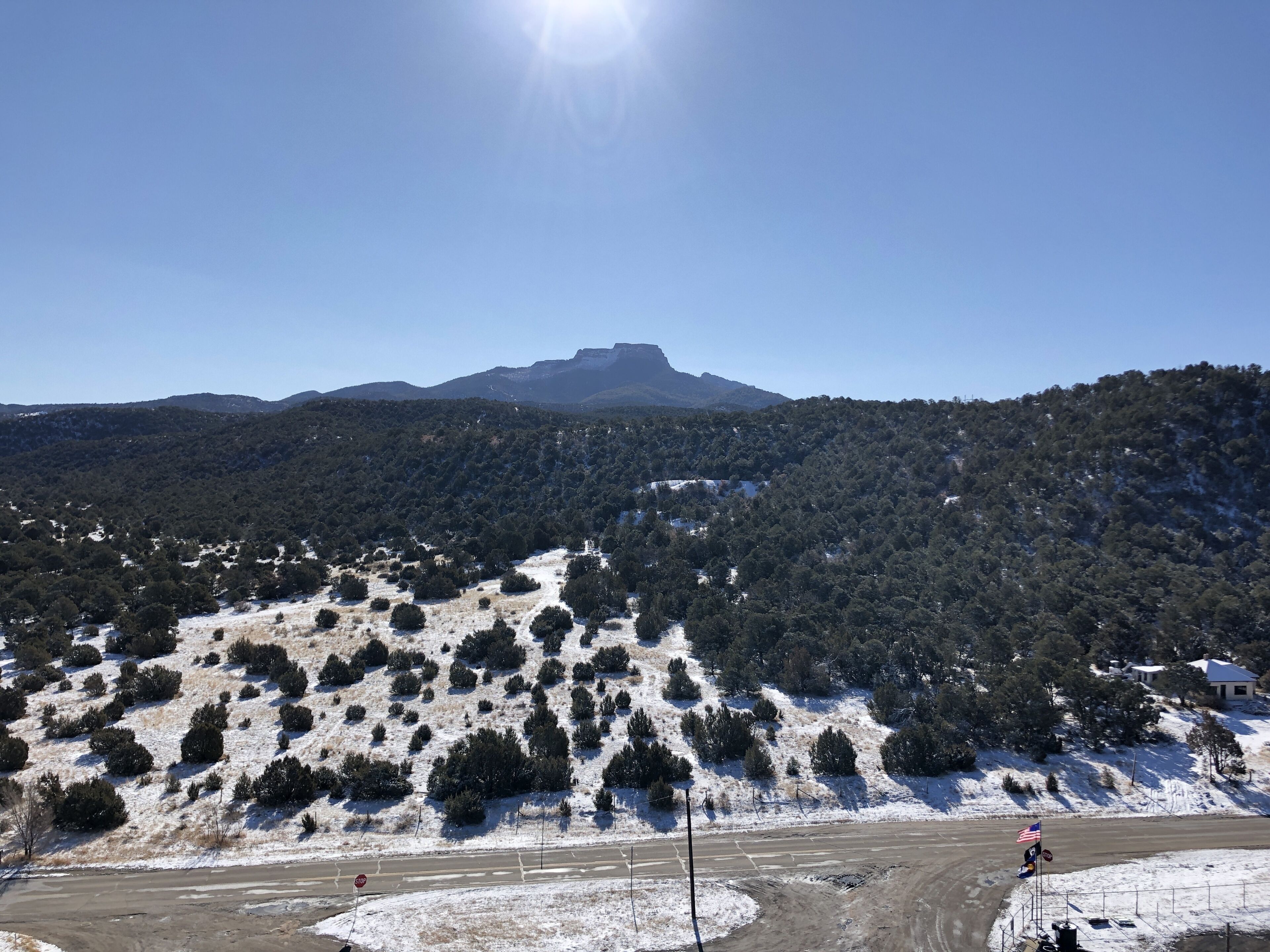 A clear view of a mountainous landscape with a road leading towards a hill with a flag.