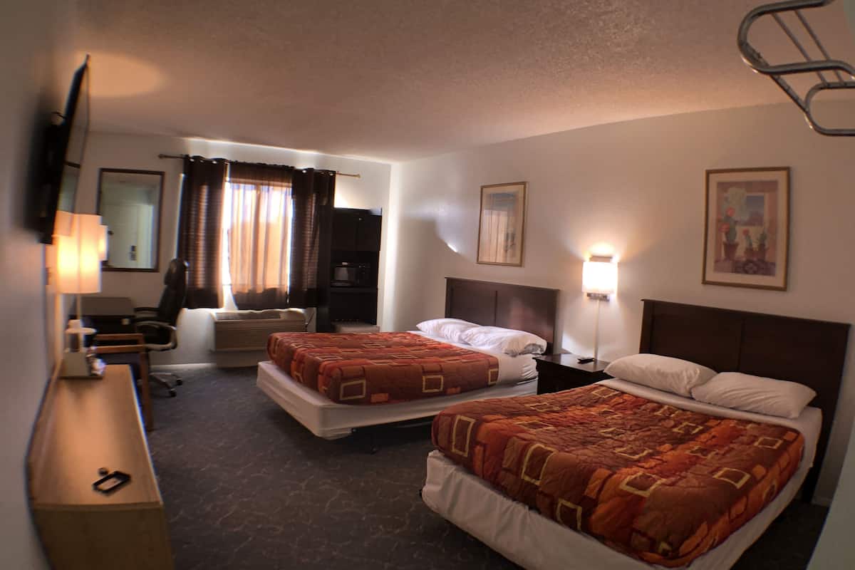 A hotel room with two beds, a desk, a chair, a TV, and a window with curtains.