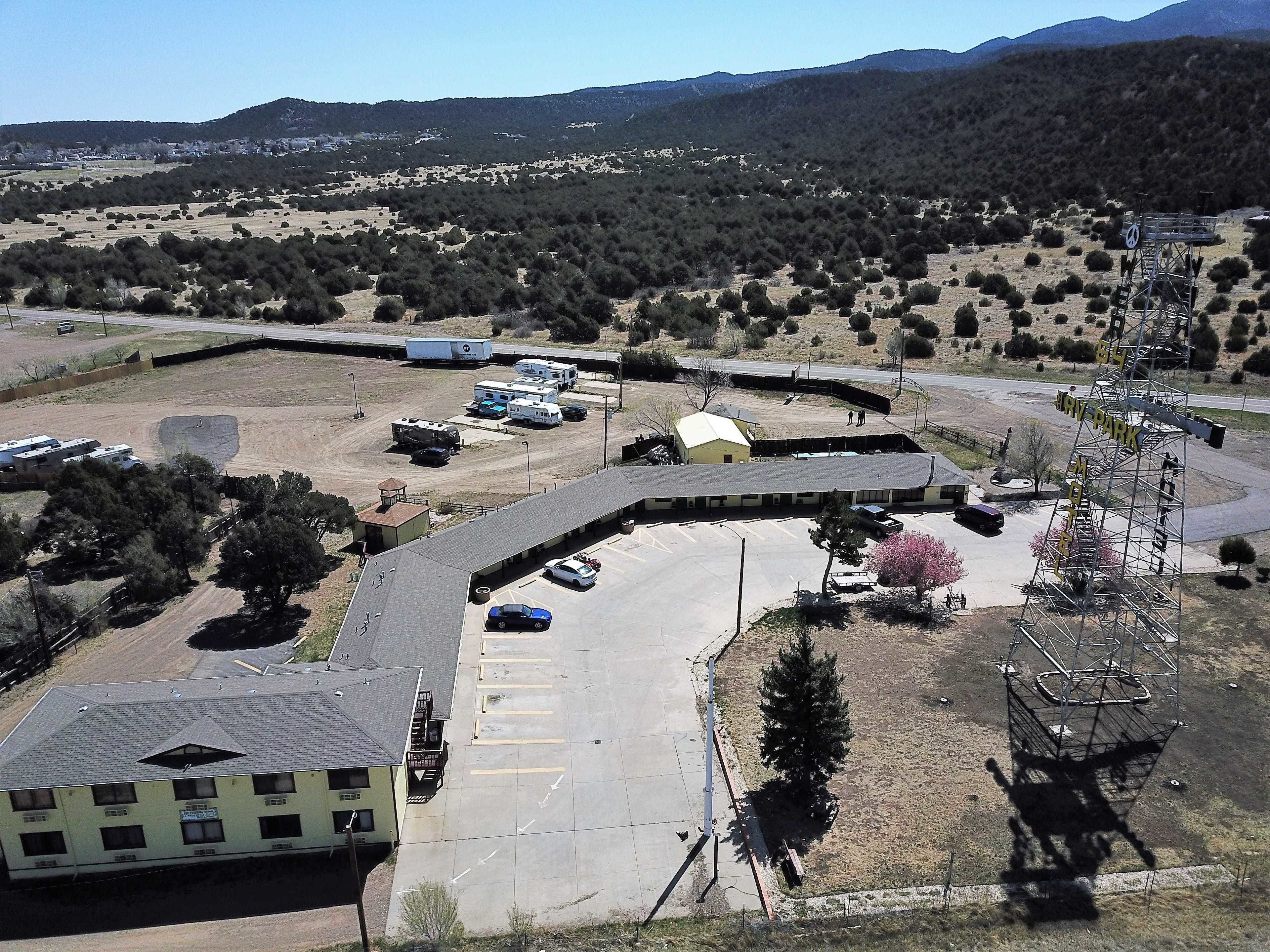 Vista aérea de un camping con espacio para vehículos recreativos, un edificio con varias ventanas y montañas al fondo.