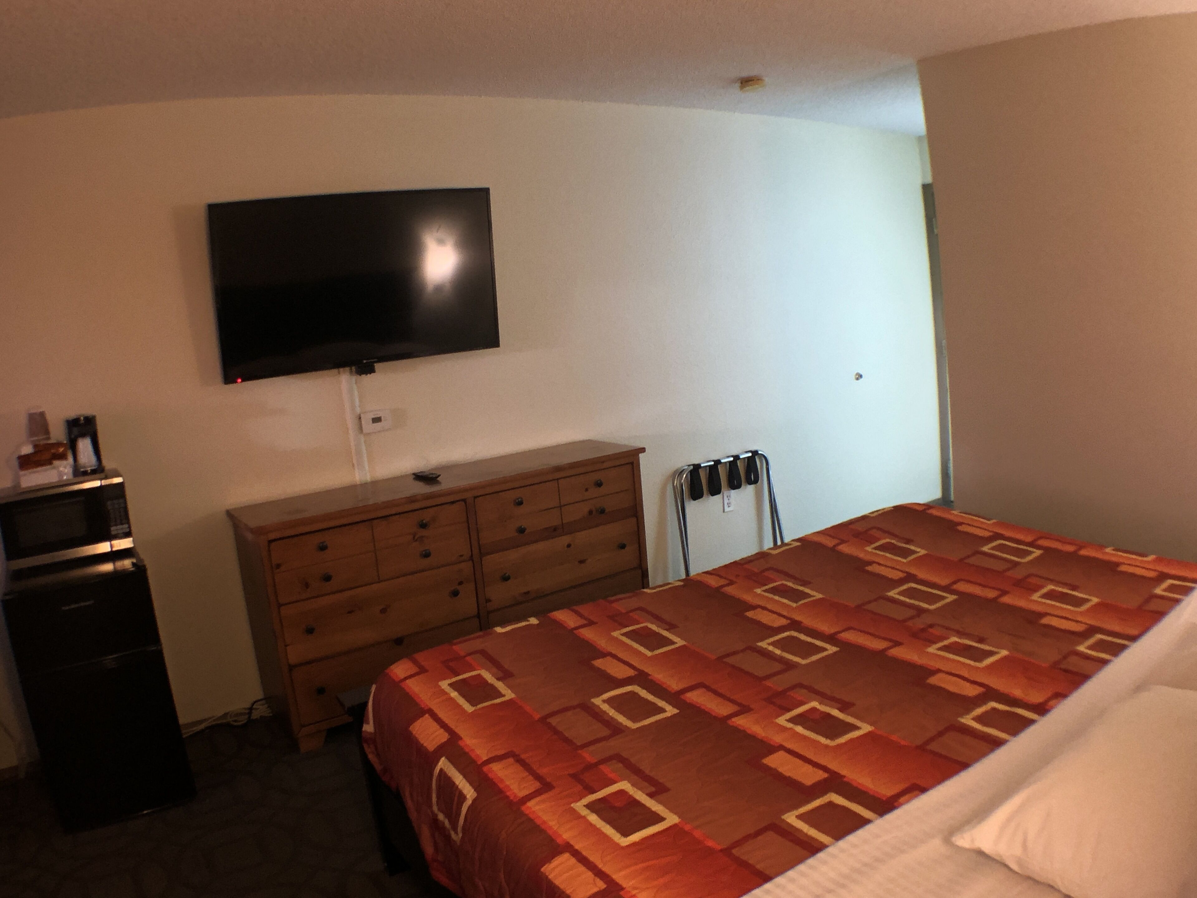 A hotel room with a bed, a dresser, a microwave, a television, and a chair.