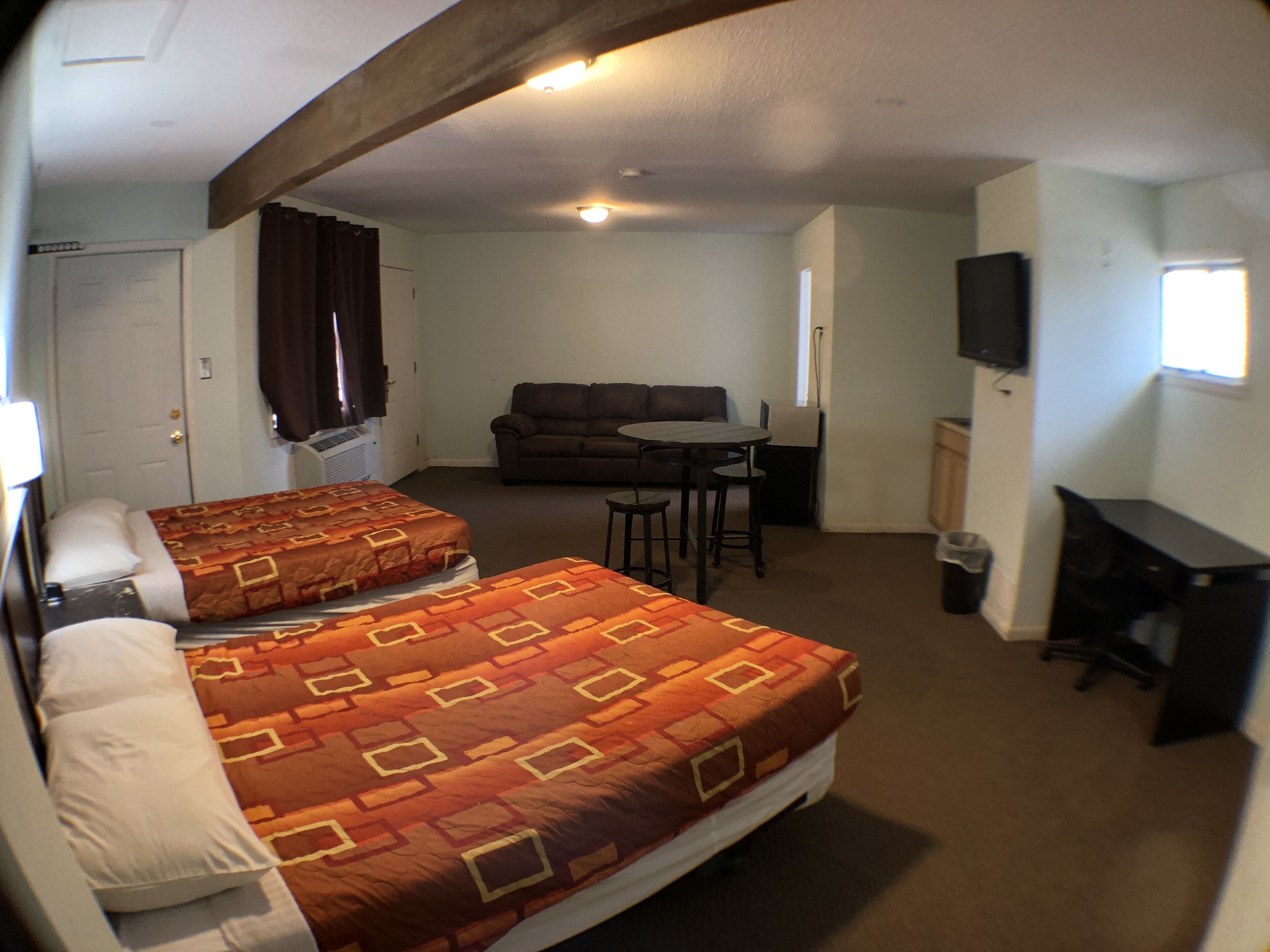 A hotel room with two beds, a sofa, a dining table, and a TV.